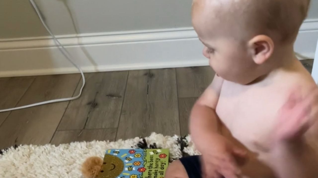 Cute little baby wants his mother to read him his favourite book by pointing at the pages