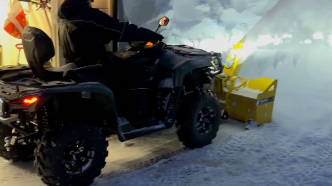 Man uses ATV with a massive snow blodet in the front to remove the snow
