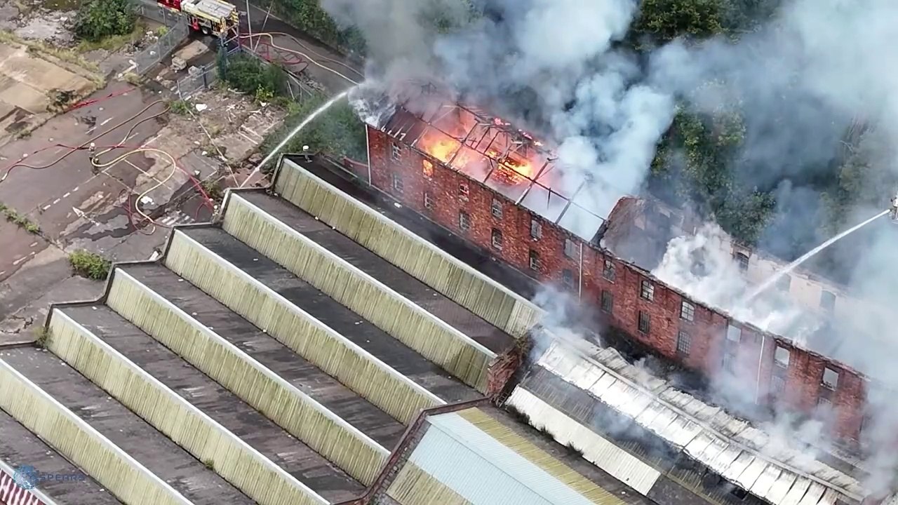 Flames and smoke pour from roof of factory building